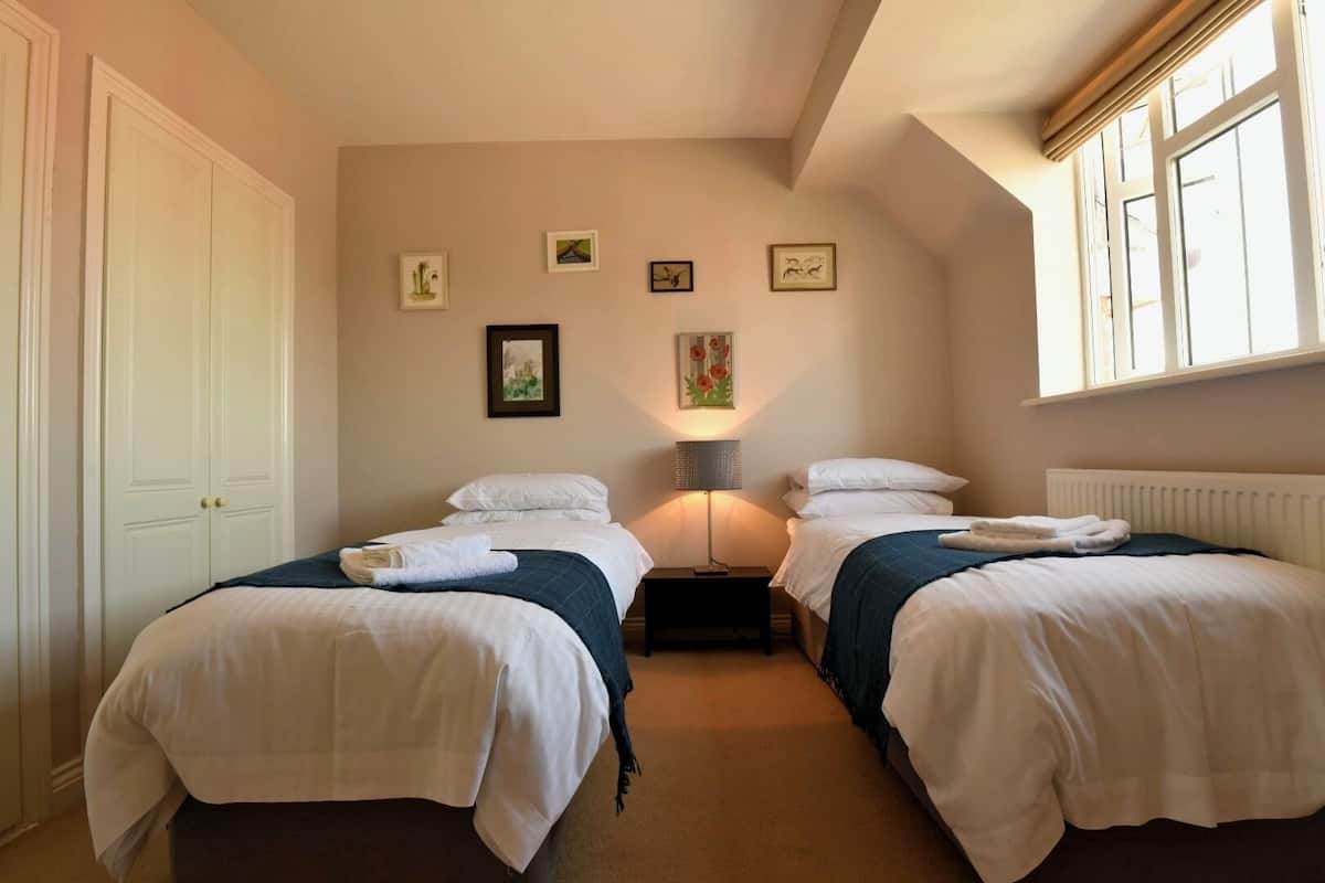 A hotel room with two beds, a nightstand, a lamp, and artwork on the wall.