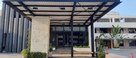 A modern building with a covered entrance, a stone pillar, and a bench.