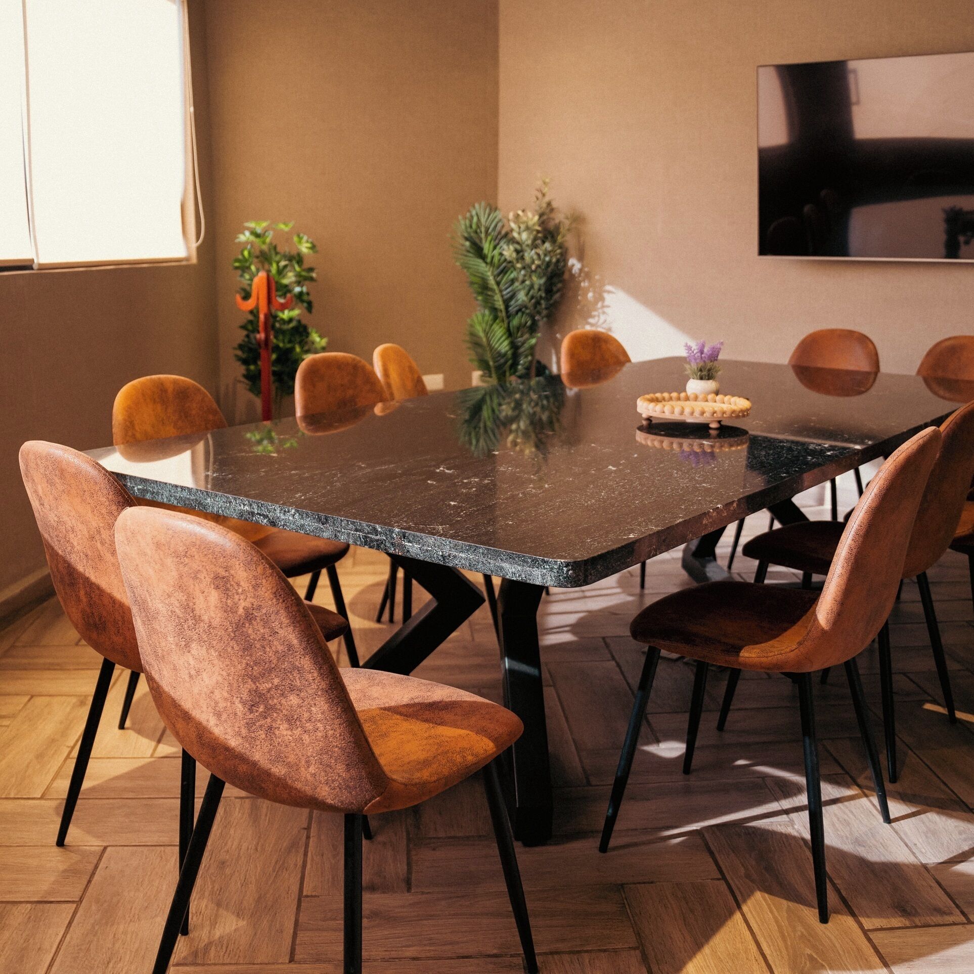 A dining area with a rectangular table, six chairs, a small potted plant, and a television mounted on the wall.