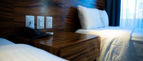 Habitación de hotel con cabecera de madera, una mesita de noche con teléfono y cama con ropa blanca.
