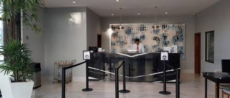 A modern lobby with a reception desk, black stanchions, and a large abstract painting on the wall.