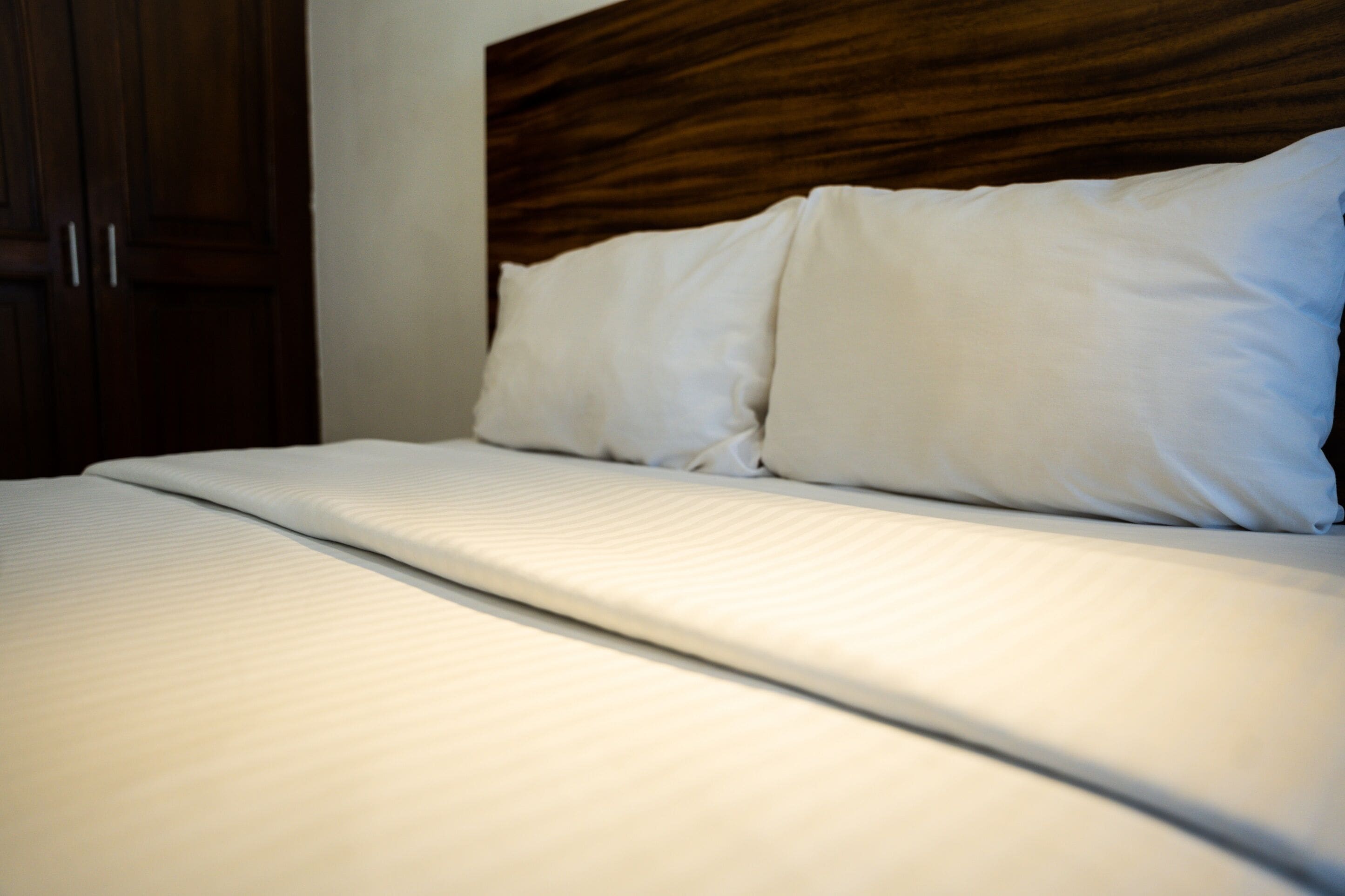 A neatly made bed with white linens and a wooden headboard.