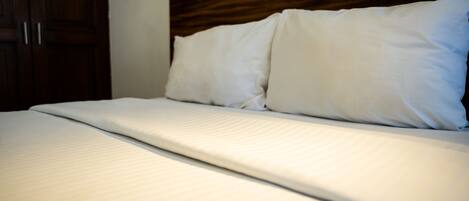 A neatly made bed with white linens and a wooden headboard.