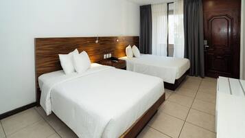 Een hotelkamer met twee bedden, een houten hoofdbord, een nachtkastje, een bureau en een grote deur.