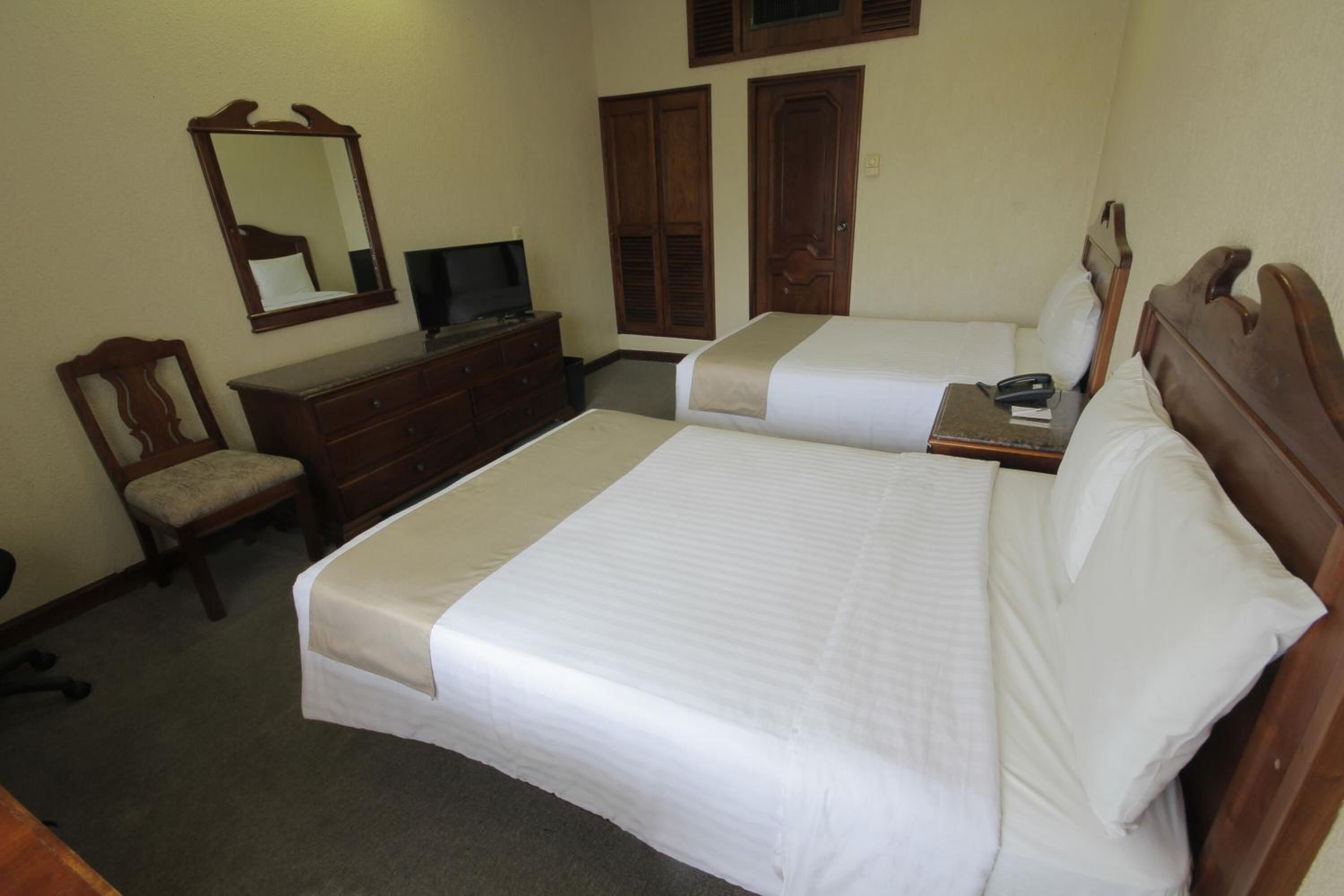 Una habitación de hotel con dos camas, un aparador, una silla, un televisor y armarios de madera.