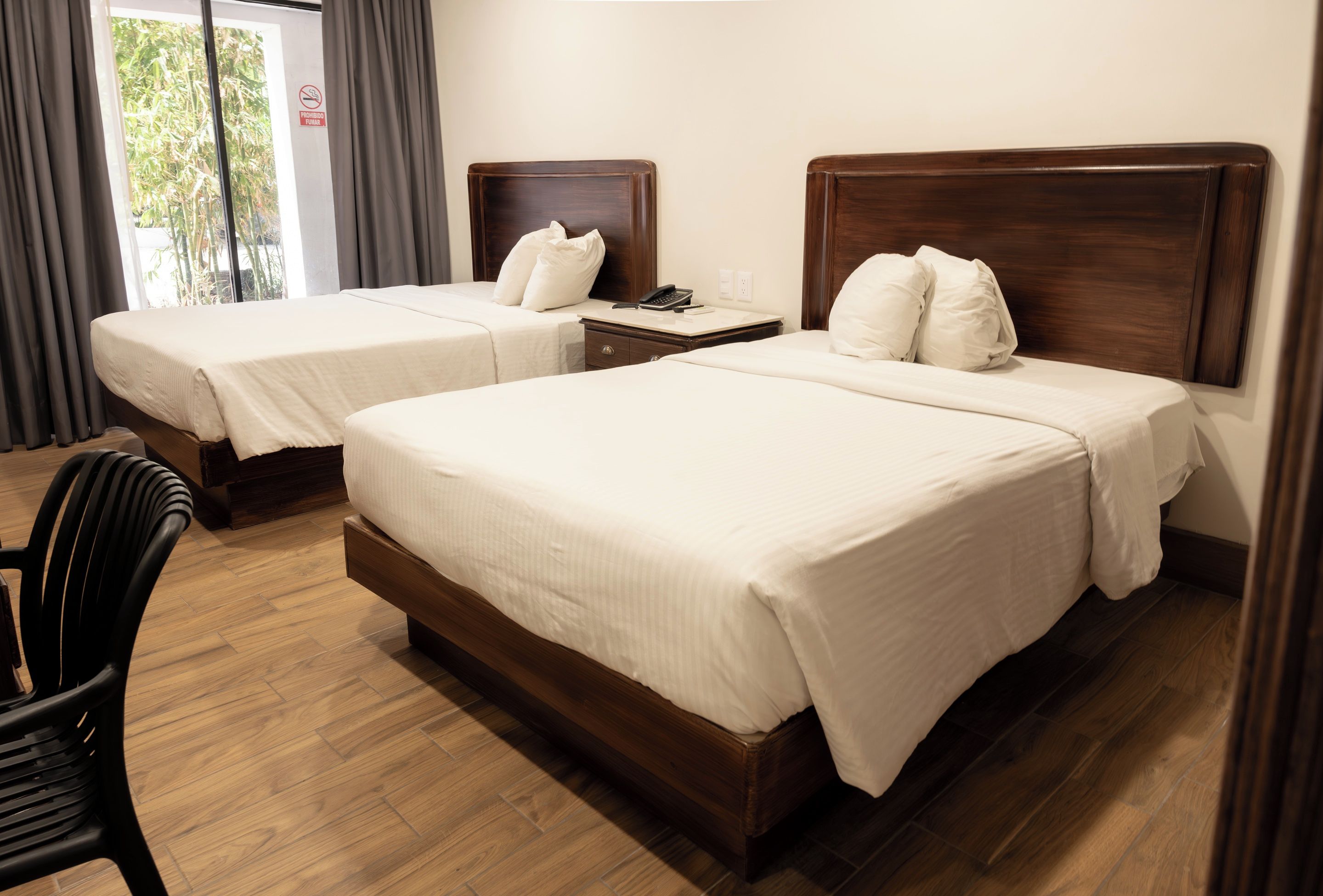 Habitación de hotel con dos camas, suelo de madera, una silla y una ventana con cortinas.