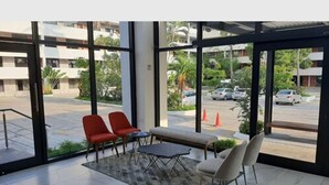 Un área de estar interior moderna con un banco, dos sillas rojas y una mesa.