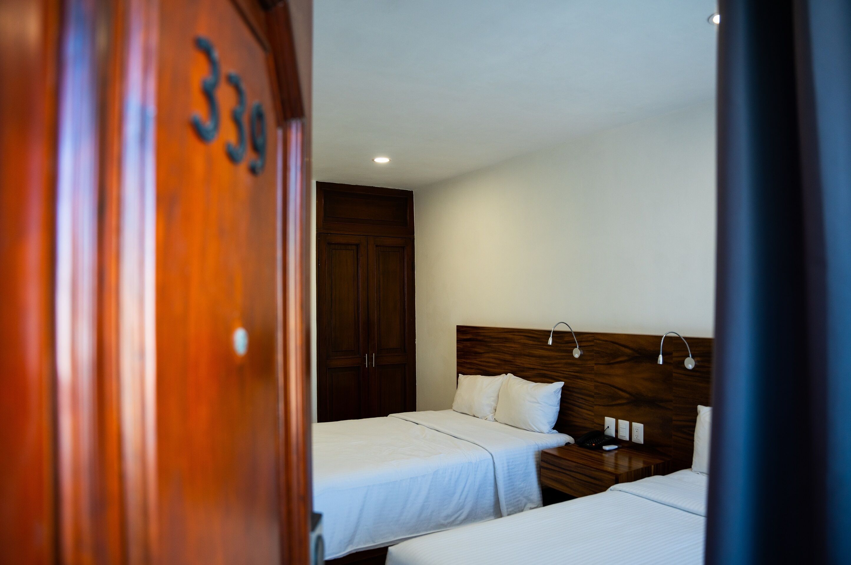 A hotel room with two beds, a wooden wardrobe, and a nightstand with a lamp.