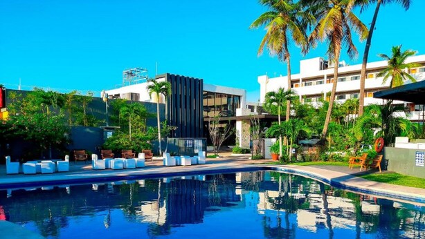 Un hotel moderno con piscina, palmeras y un cielo azul despejado.