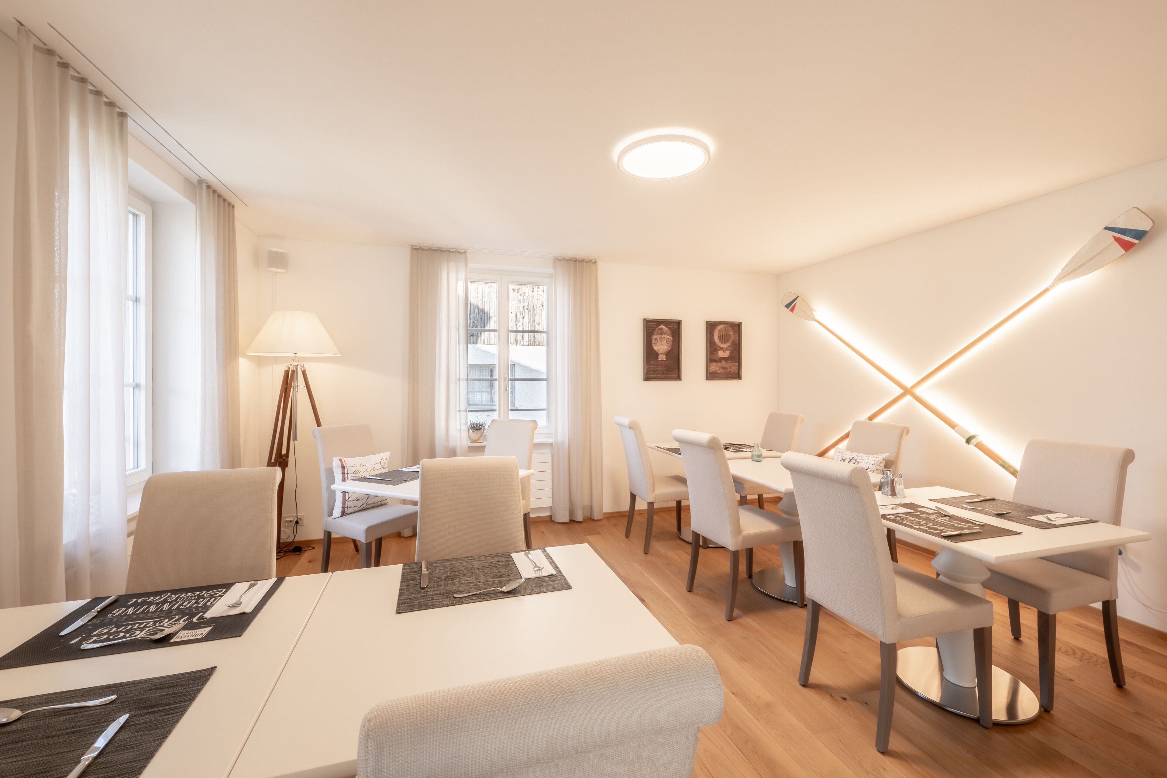Un comedor moderno con mobiliario blanco, una mesa dispuesta para dos personas y una lámpara de pie.