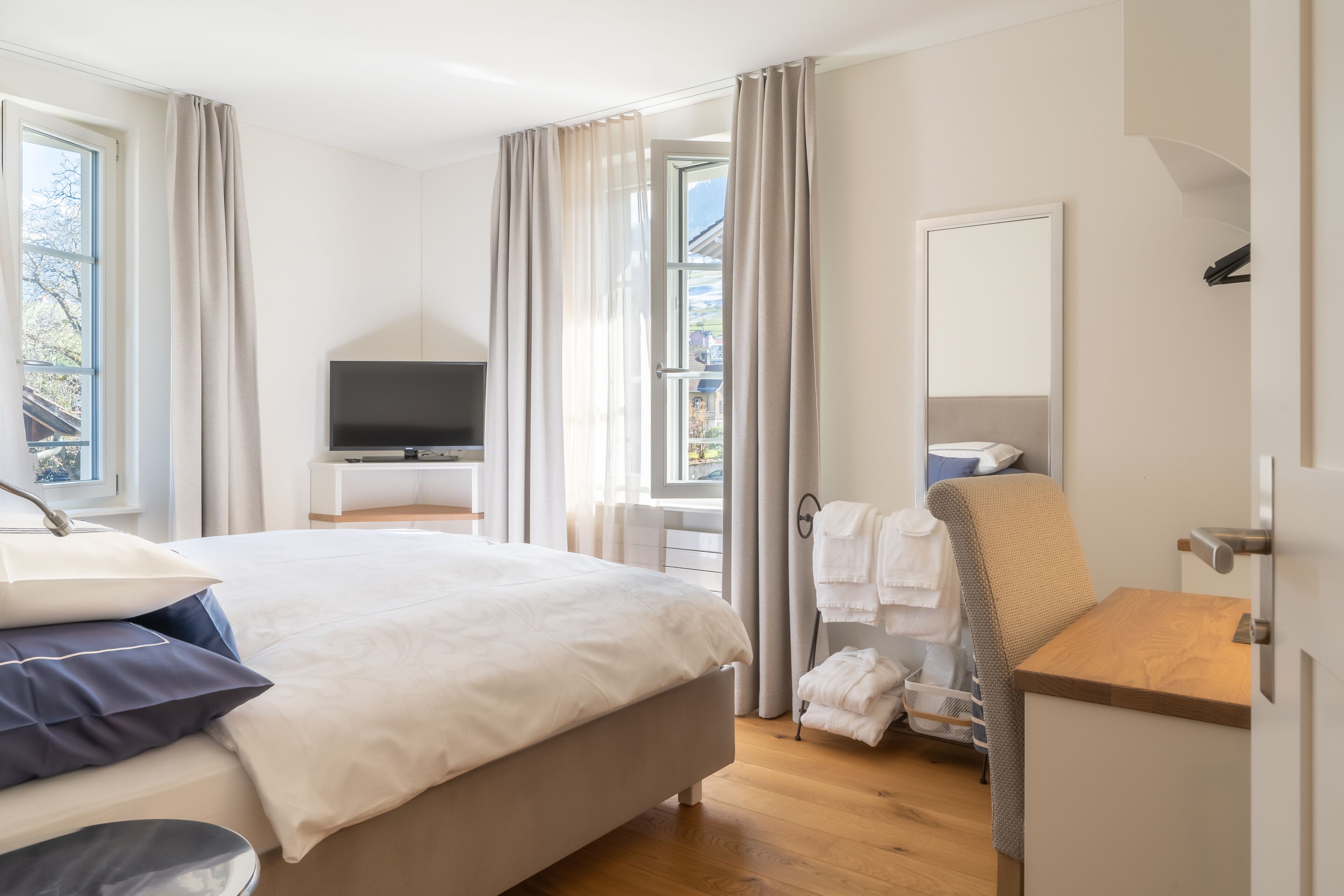 Une chambre d’hôtel moderne avec un grand lit, une télévision, une table de chevet en bois et une vue sur l’extérieur.