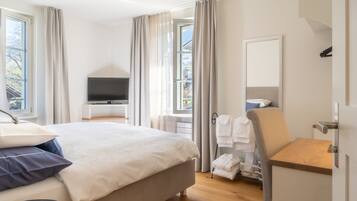 Une chambre d’hôtel moderne avec un grand lit, une télévision, une table de chevet en bois et une vue sur l’extérieur.