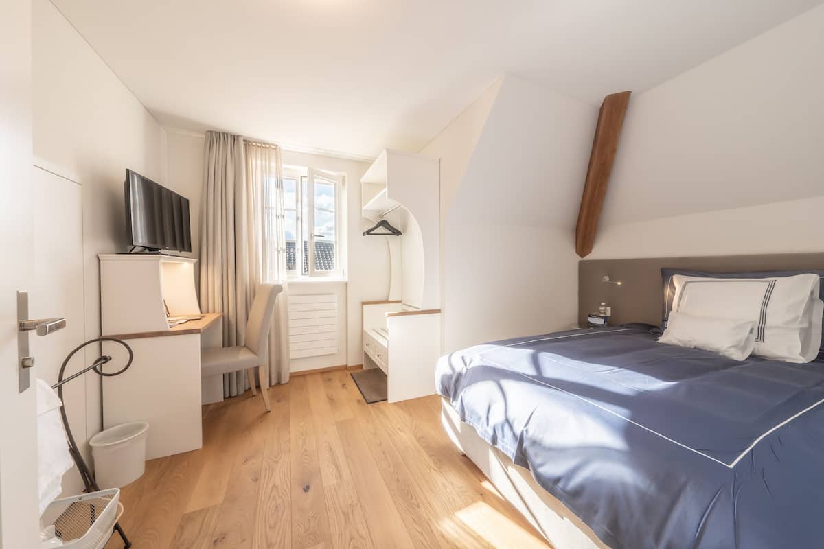 Hotellihuone, jossa on sänky, työpöytä, tuoli, televisio ja ikkuna, jossa on verhot.