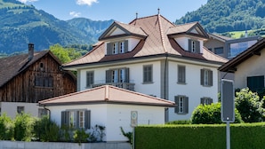 A two-story house with a sloped roof, multiple windows with shutters, and a visible chimney.