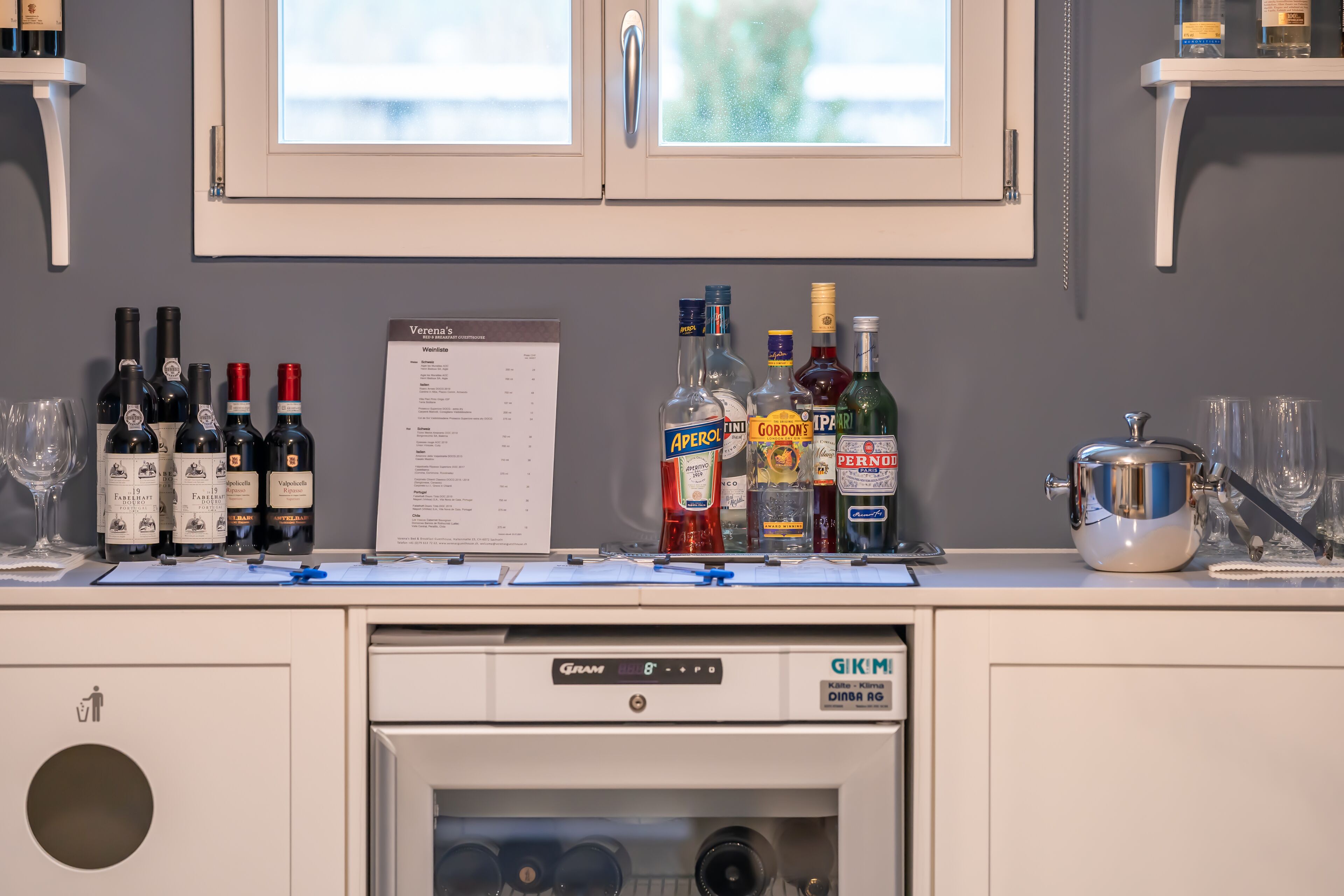 Un espace bar avec différentes bouteilles d’alcool, un menu et un lave-vaisselle.