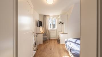 A compact bedroom with a bed, a desk with a chair, a TV, and a window with curtains.