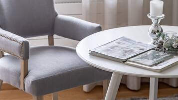 A room with a grey upholstered chair, a white round table with a candle and decorative items, and a grey carpet.