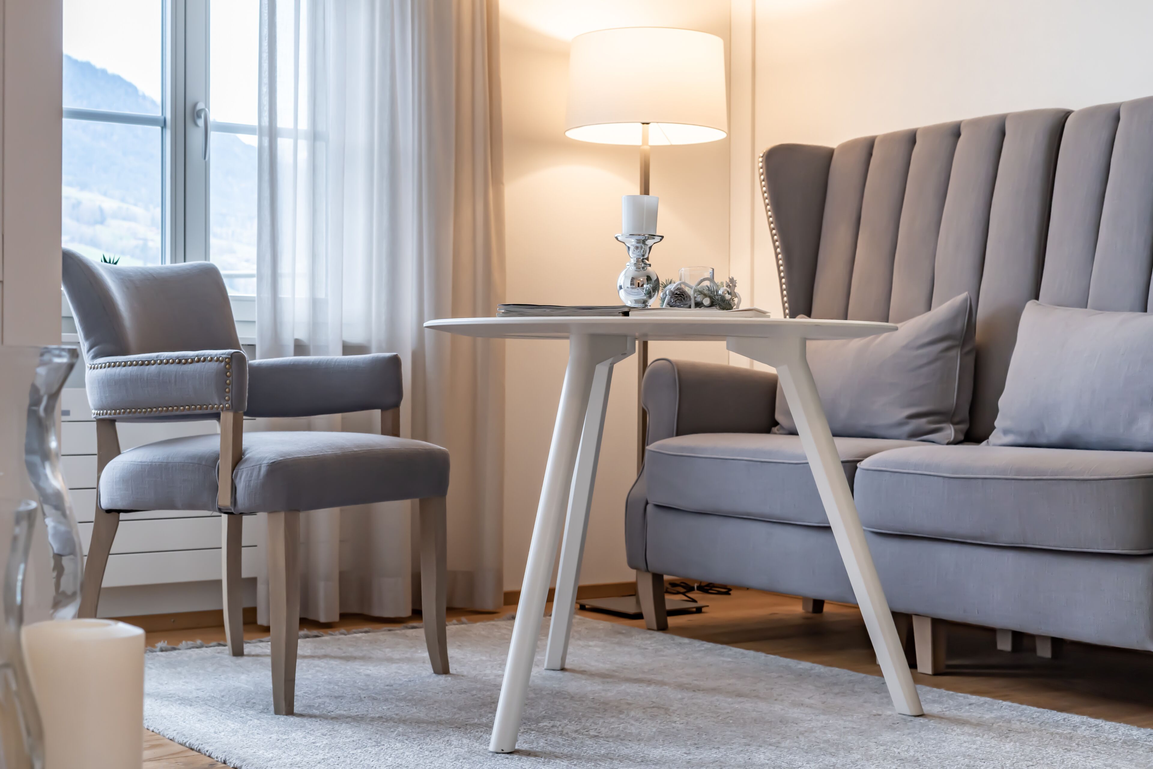 Un salon moderne avec un canapé gris, deux fauteuils, une petite table blanche et un lampadaire.