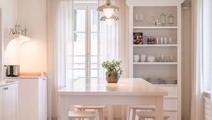 A modern kitchen with white cabinetry, a central island with stools, pendant lighting, and a view through large windows.