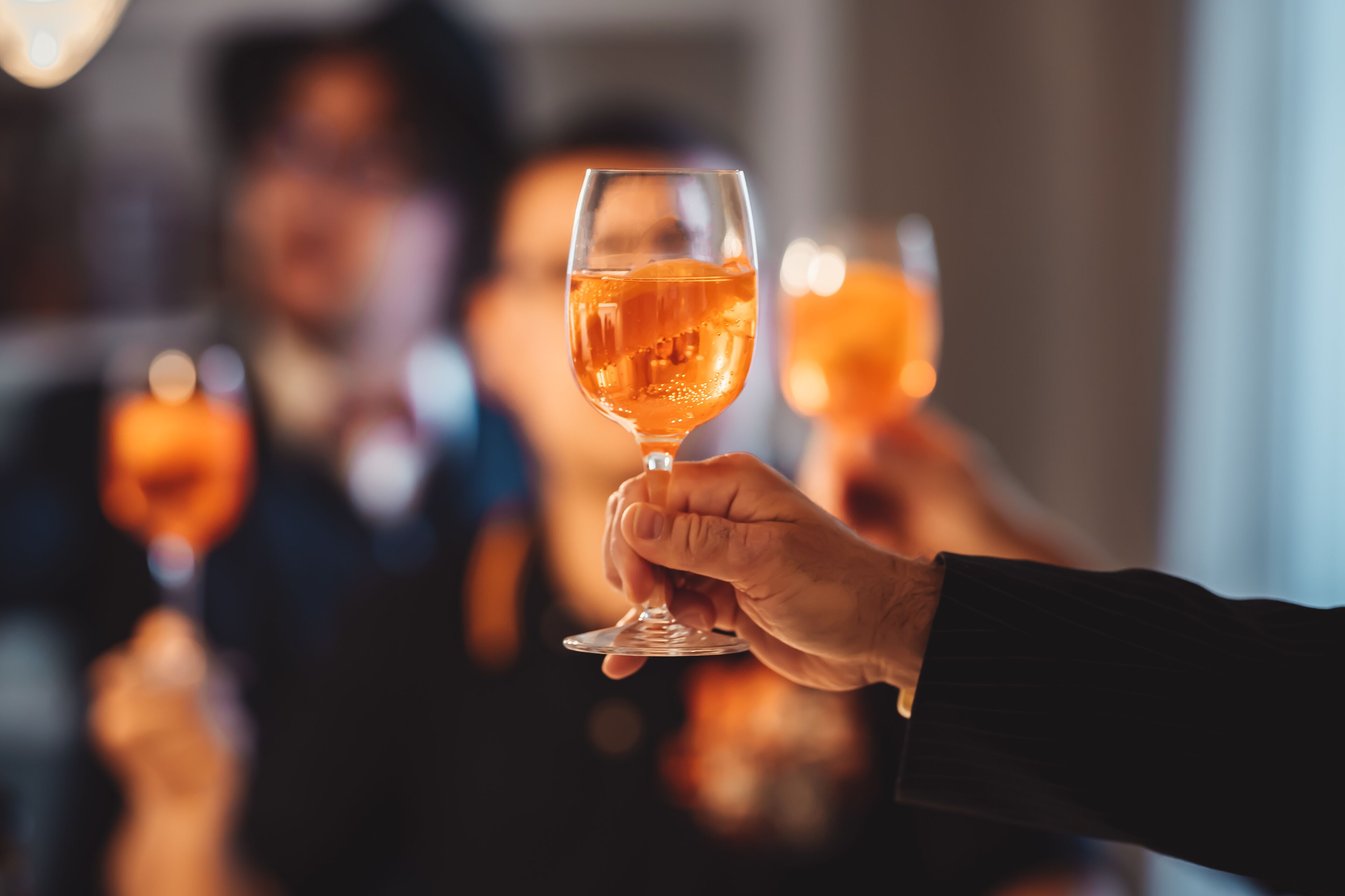 A person holding a glass of amber liquid, likely a beverage, in a well-lit indoor setting.