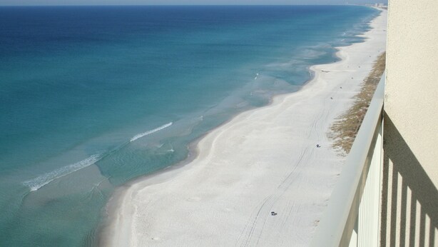 En vy över en strand sedd från luften, med kristallklart turkosfärgat vatten och en sandstrand.