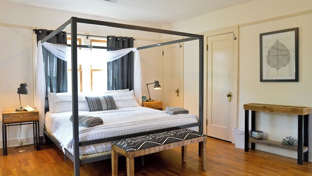 A four-poster canopy bed with a wooden bench, bedside tables, and a small console table with a decorative item. - The Riverpath Inn, just steps from the Willamette river & Rose Gardens, Eugene (Eugene)