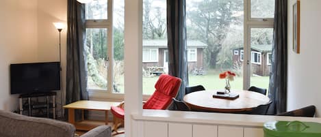 A living room with a television, a sofa, a dining table with chairs, and a view of the outside.