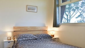 A bedroom with a bed, two bedside tables, a nightstand, a drawer unit, a framed picture on the wall, and a window with curtains.