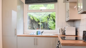 A modern kitchen with white cabinets, a window with a view of greenery, a kettle, a microwave, and a coffee maker.