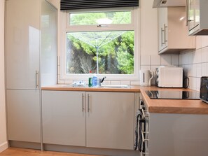 A modern kitchen with white cabinets, a window with a view of greenery, a kettle, a microwave, and a coffee maker. - 2 bedroom accommodation in Mount Hawke, near Redruth (Mount Hawke, near Redruth)