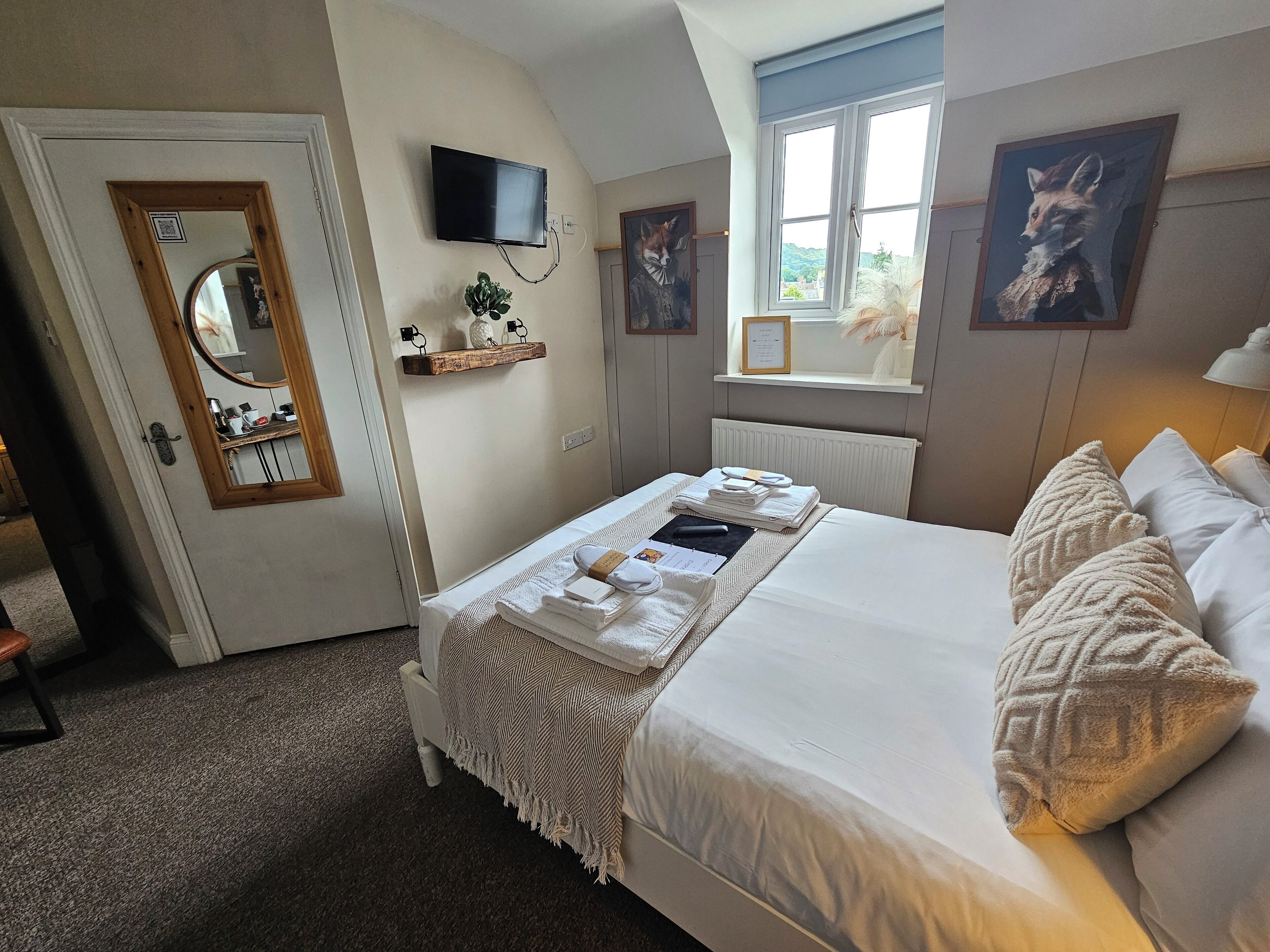 Une chambre bien rangée, avec un lit, une télévision, une fenêtre donnant sur un beau paysage et un miroir.