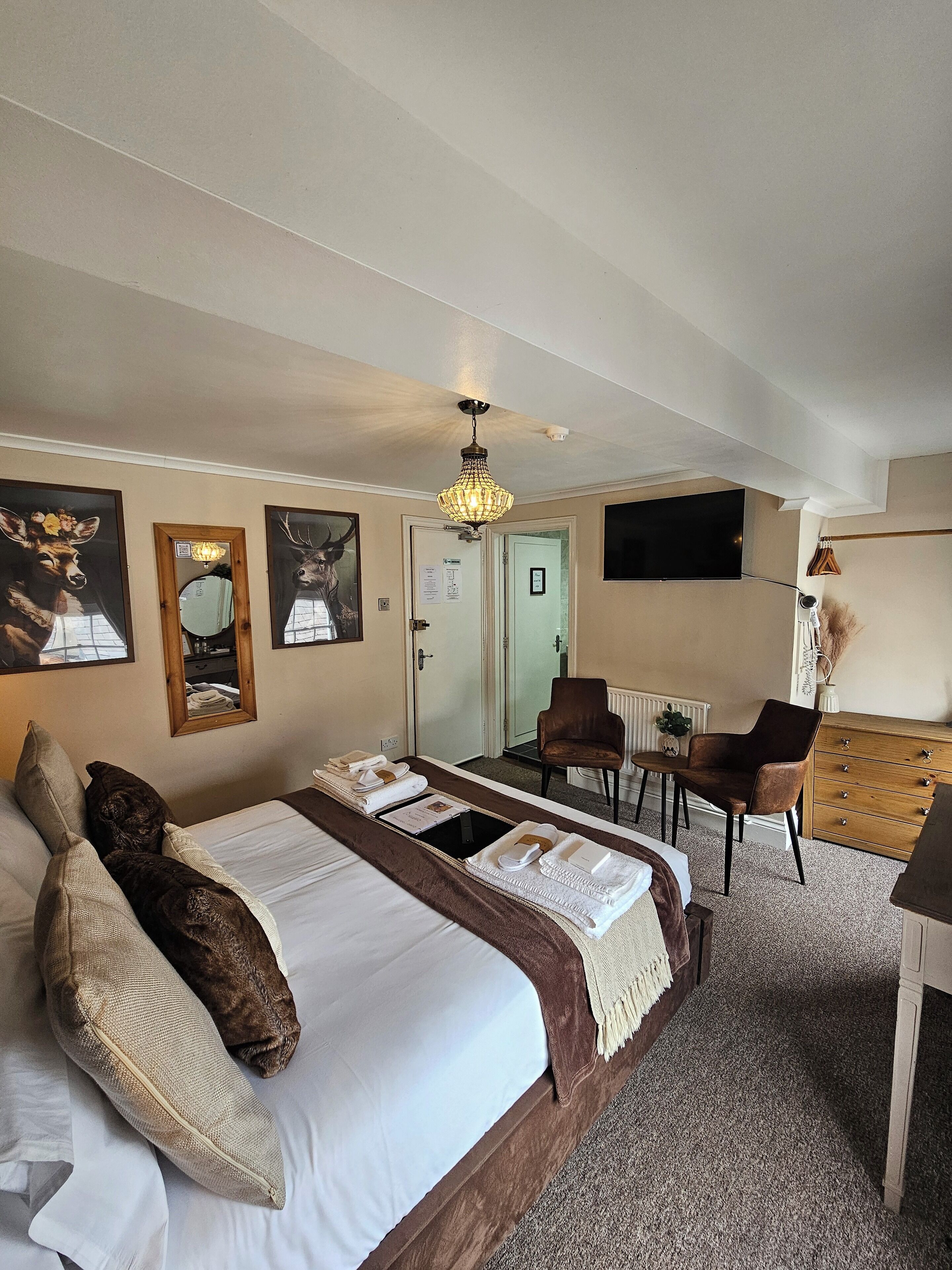 A hotel room with a large bed, a desk, a chair, and a television mounted on the wall.