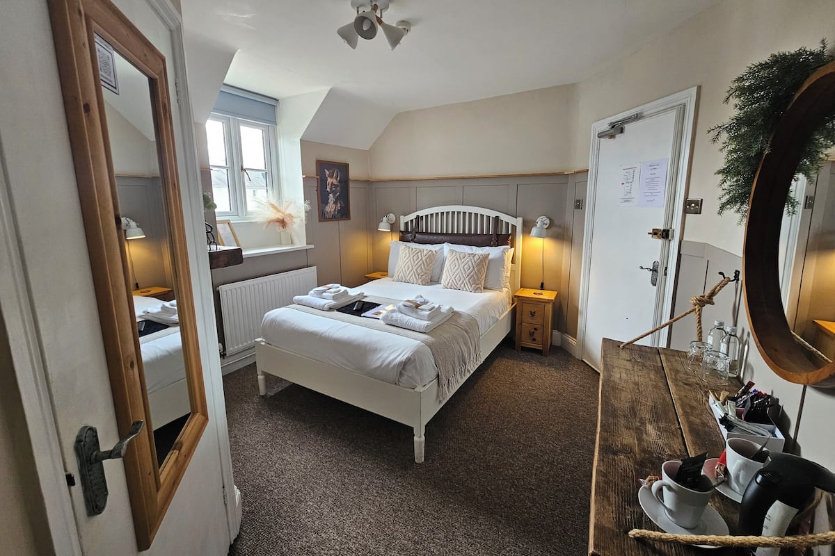 A neatly arranged bedroom with a bed, bedside tables, a mirror, and a window.