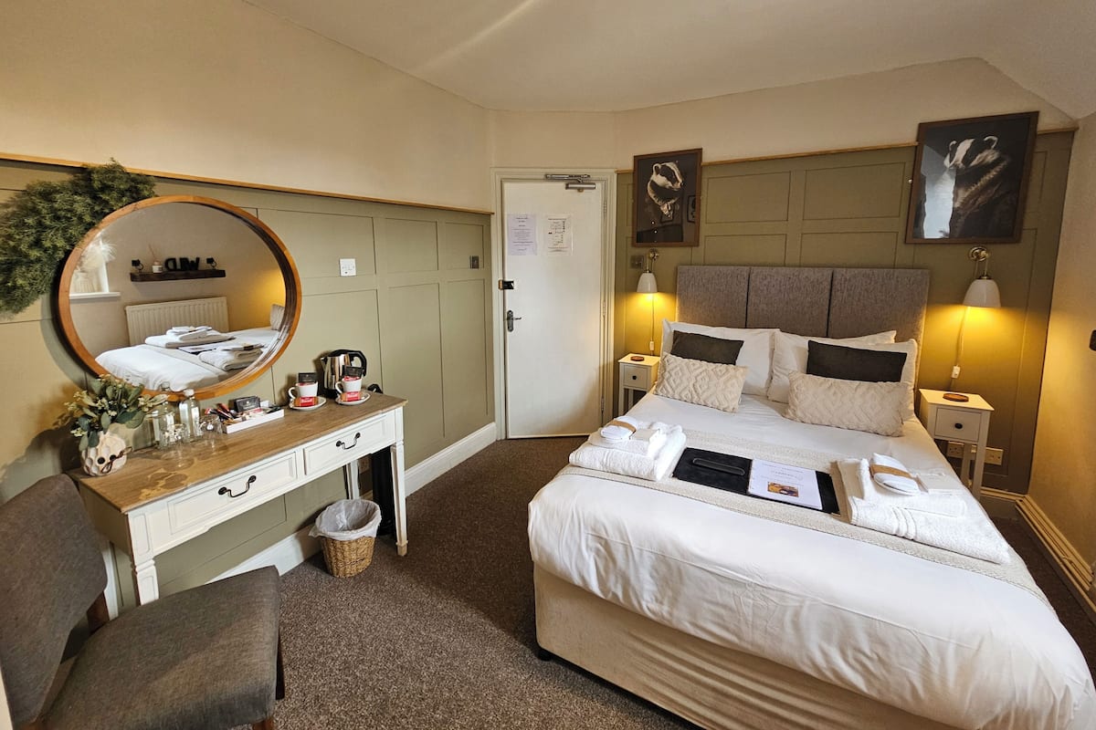 A hotel room with a bed, bedside tables, a desk with a mirror, and a chair.