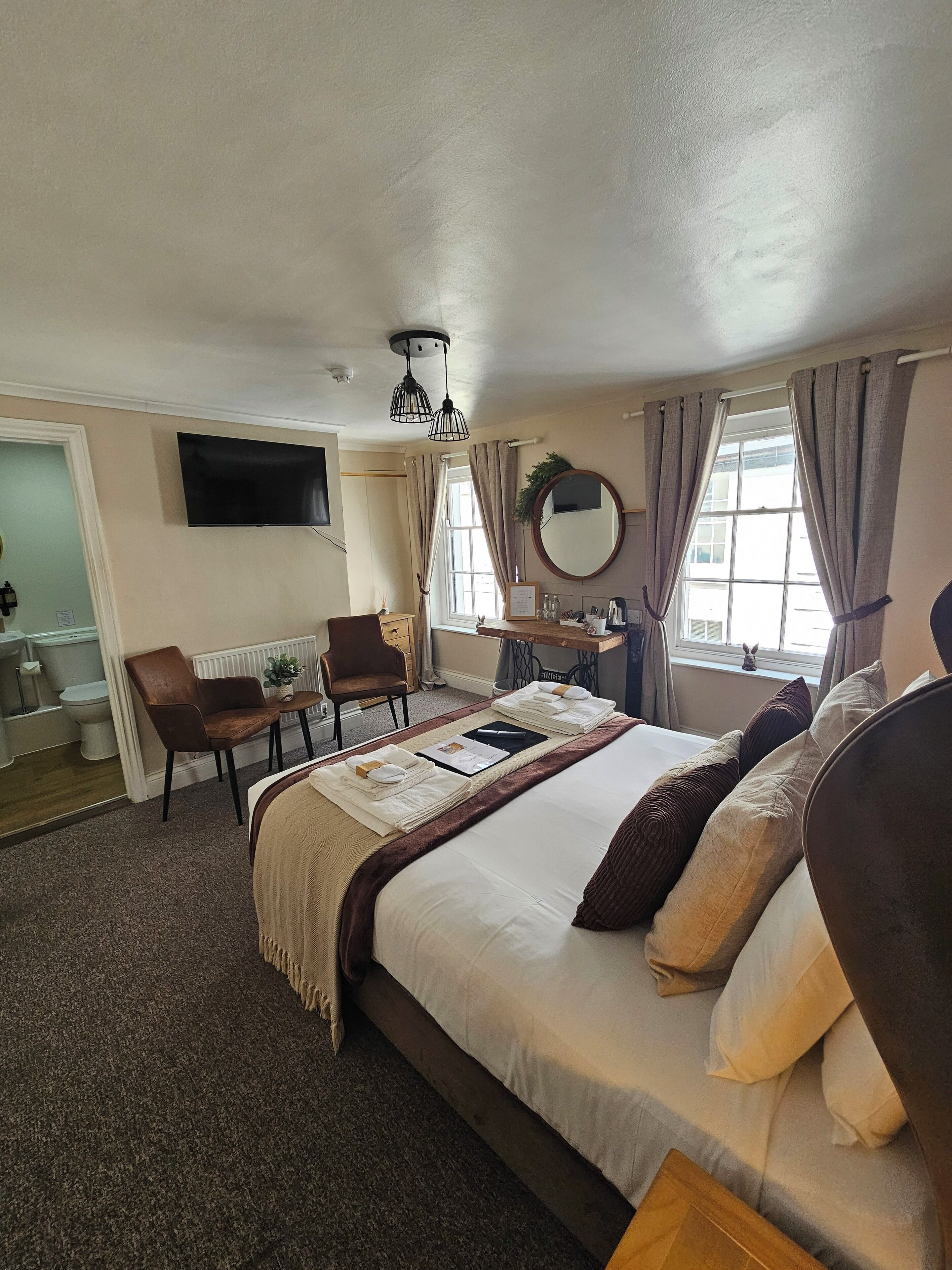 Quarto de hotel com cama, escrivaninha, cadeira, televisão e janela com cortinas.