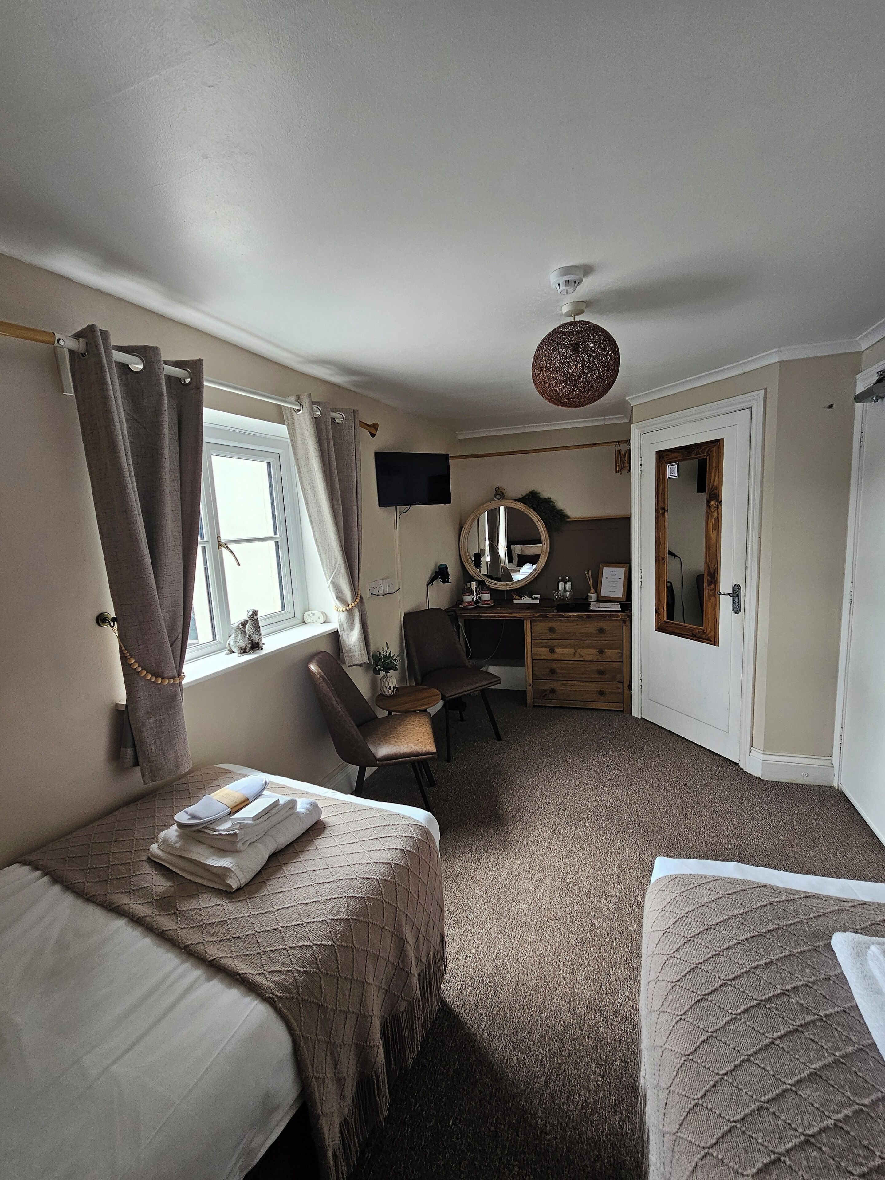 Een kamer met twee bedden, een bureau, een stoel, een spiegel en een raam met gordijnen.