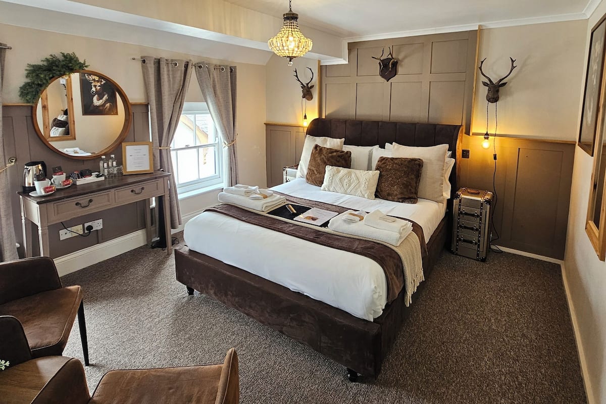A spacious bedroom with a large bed, a dresser, a mirror, and a chandelier.