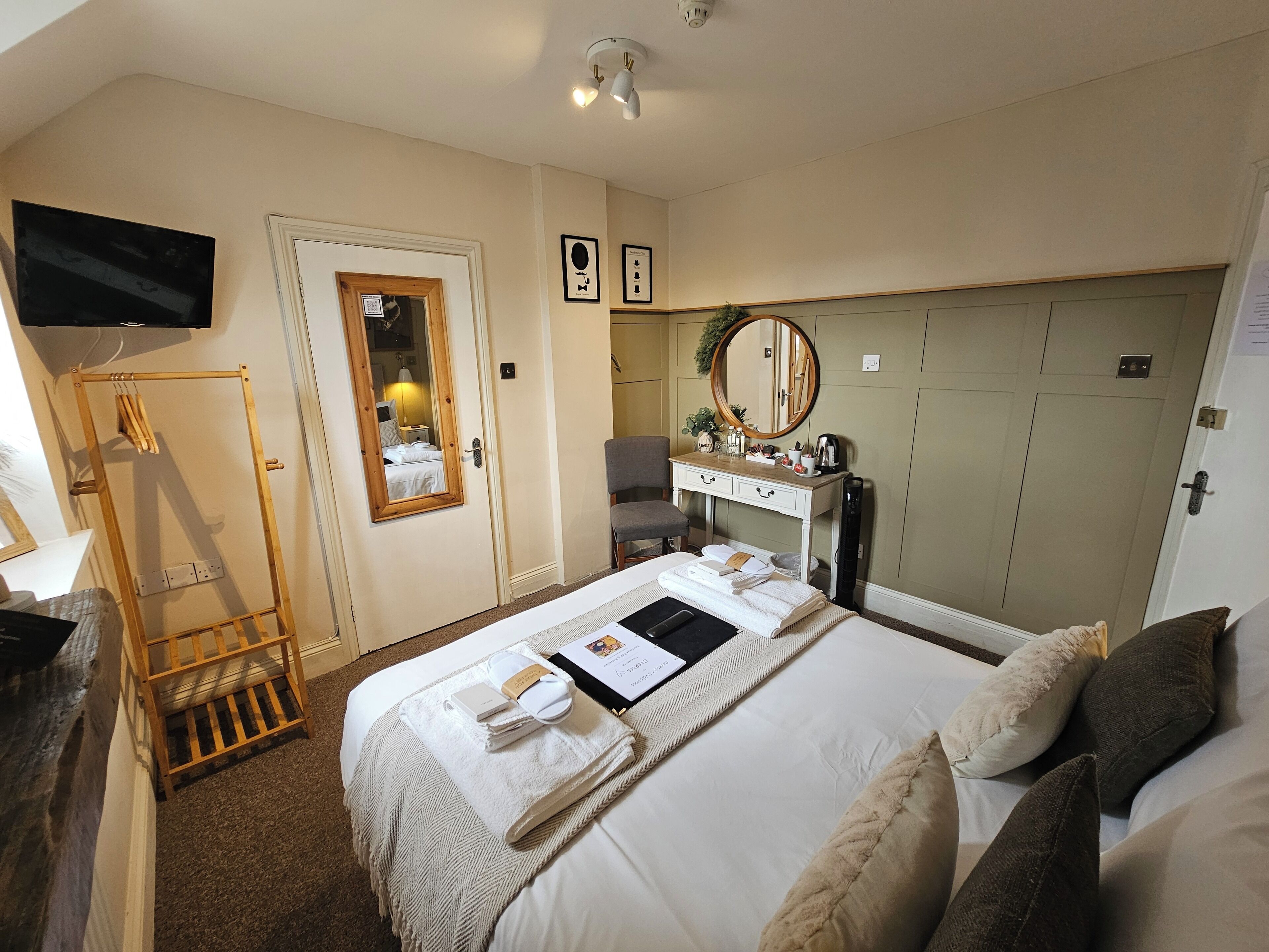 A hotel room with a bed, a desk with a mirror, a chair, and a television mounted on the wall.