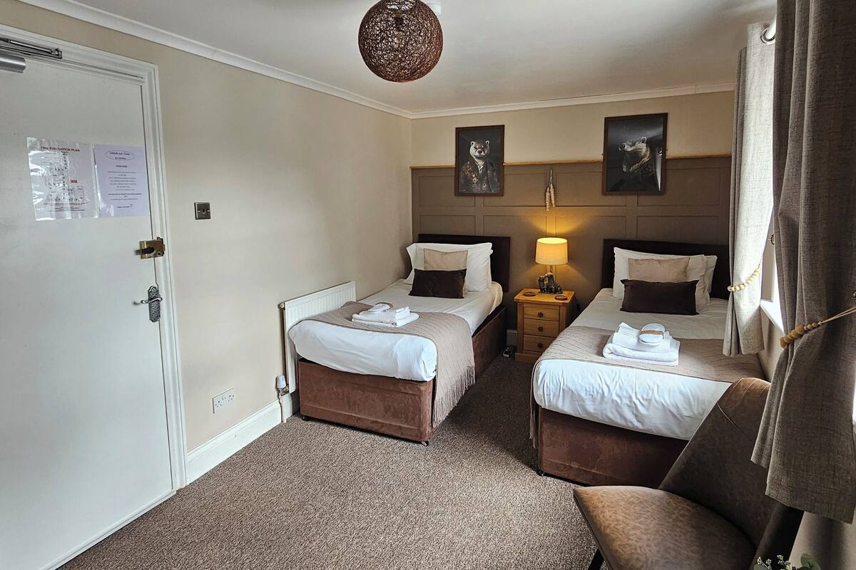A hotel room with two beds, a sofa, a small table, and a ceiling light.