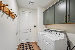 A laundry room with a white washer and dryer, wooden coat hooks, and a gray cabinet above the dryer.