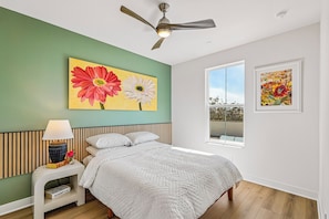 A bedroom with a bed, a nightstand, a lamp, a ceiling fan, and two wall-mounted paintings. - Brand-New 2BR/2BA at Sterling Grove. Includes Golf Cart + Resort Amenities (Surprise)