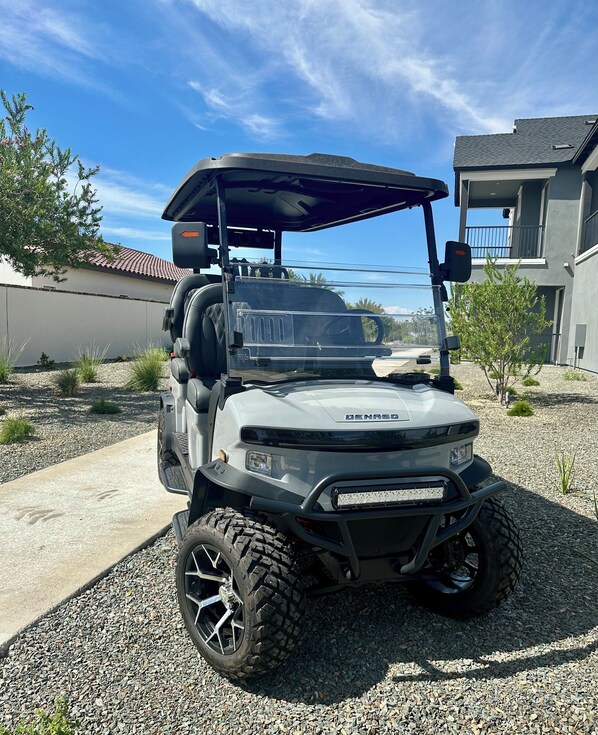 A golf cart parked on a gravel driveway with a house in the background.