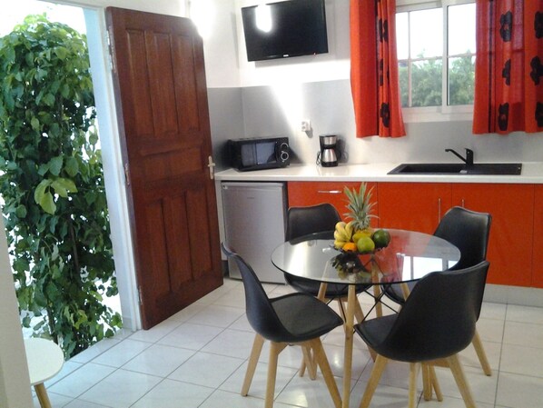 A compact kitchen with a dining area, a TV mounted above the counter, and a potted plant near the entrance. - Comfortable f2 gite with swimming pool (Le moule)