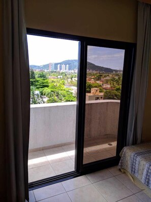 Un balcón con vistas a la ciudad, una cama y un ventanal con cortinas.
