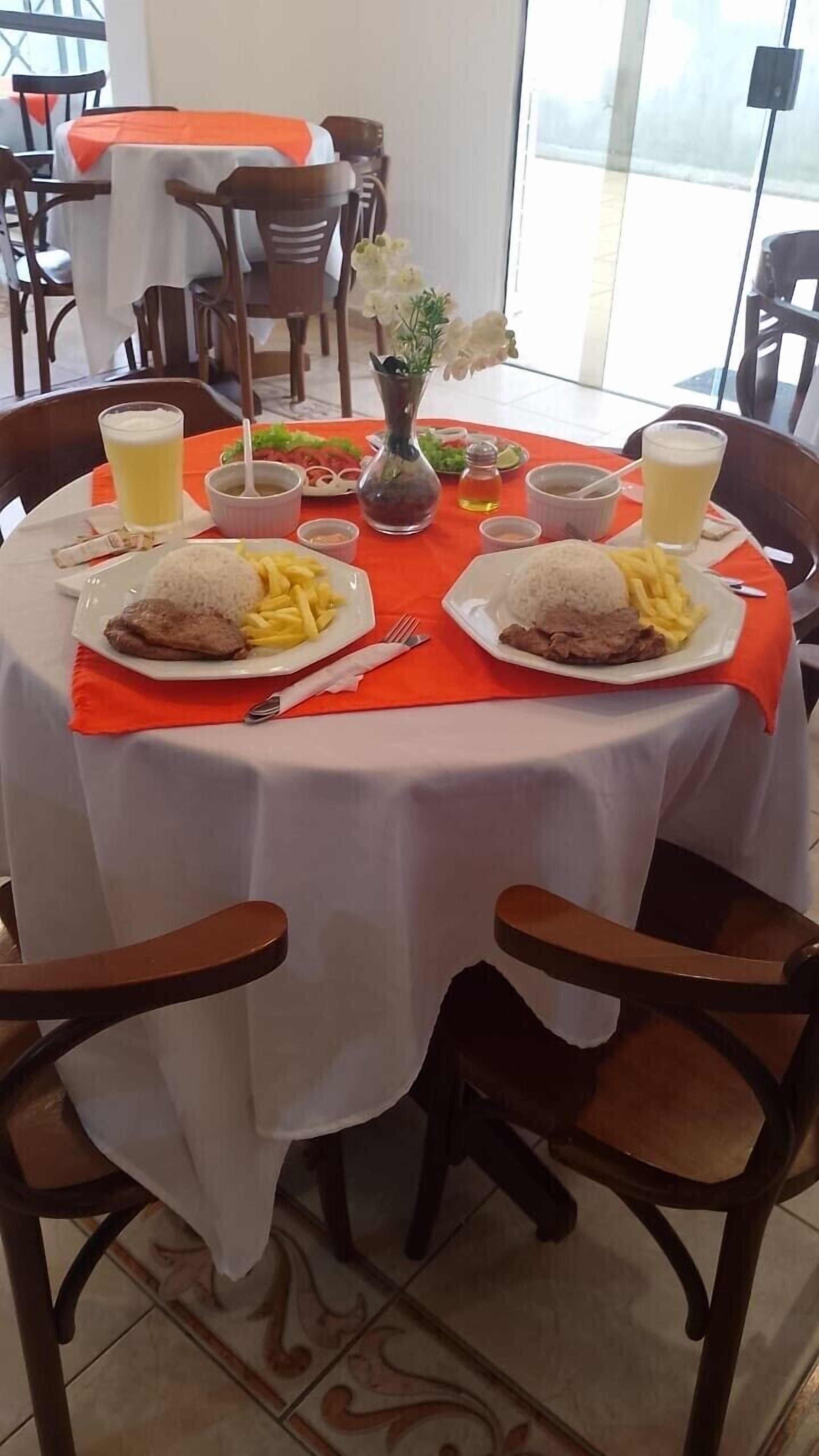 A dining table with two plates of food, including rice and meat, and two glasses of a yellow beverage.