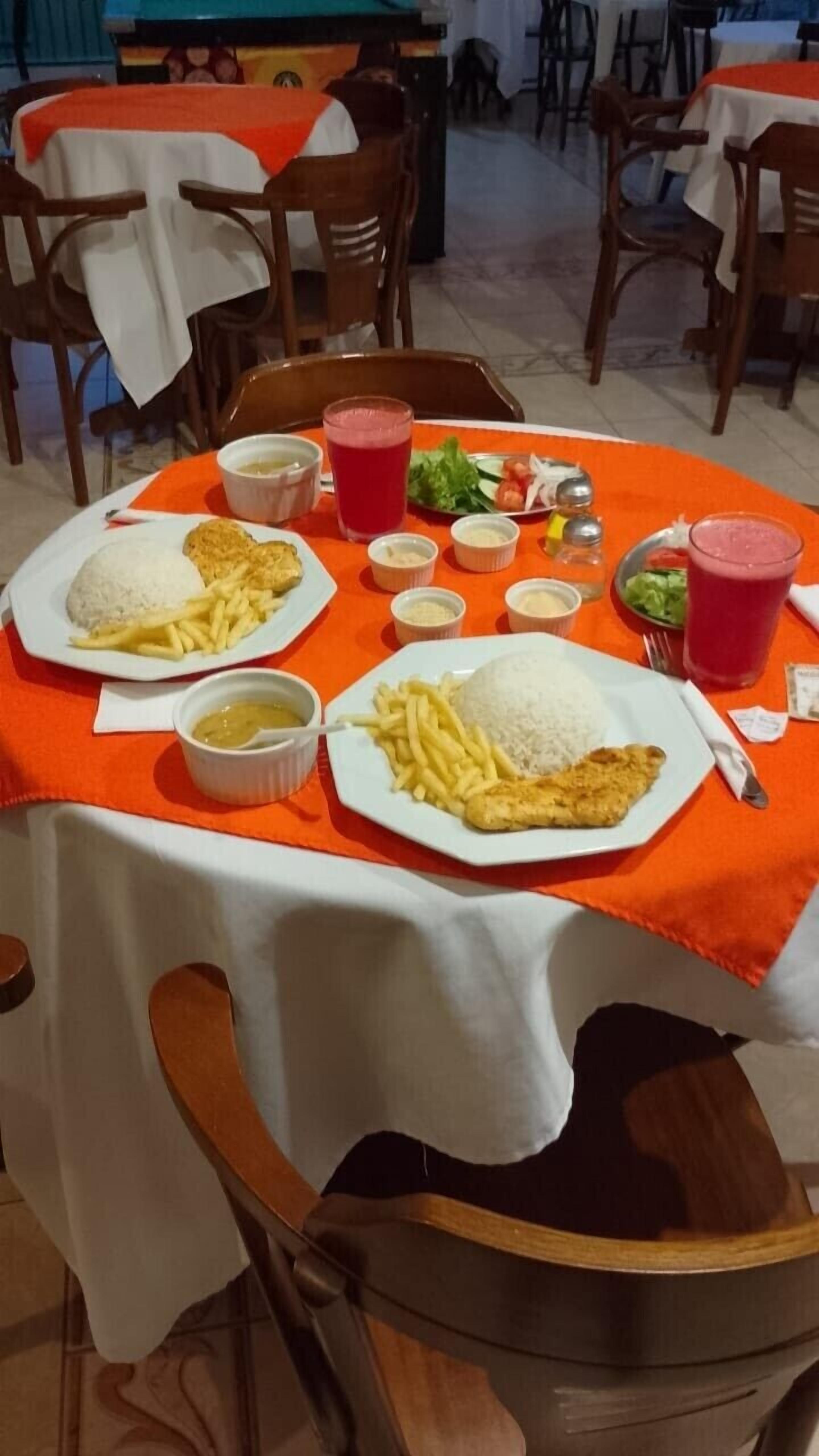 A dining table with two plates of food, including rice, fries, and a fried item, along with various condiments and a drink.