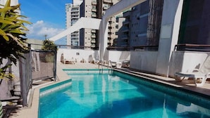 A swimming pool with lounge chairs, surrounded by high-rise buildings. - Hotel Canto do Atlântico (Guarujá)