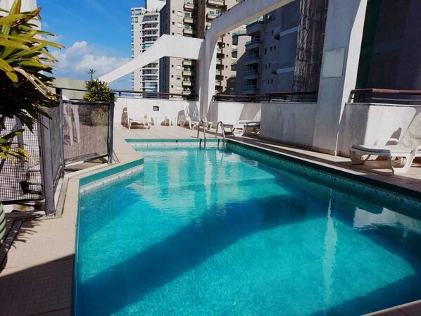 Una piscina con sillones de descanso, rodeada de edificios altos.