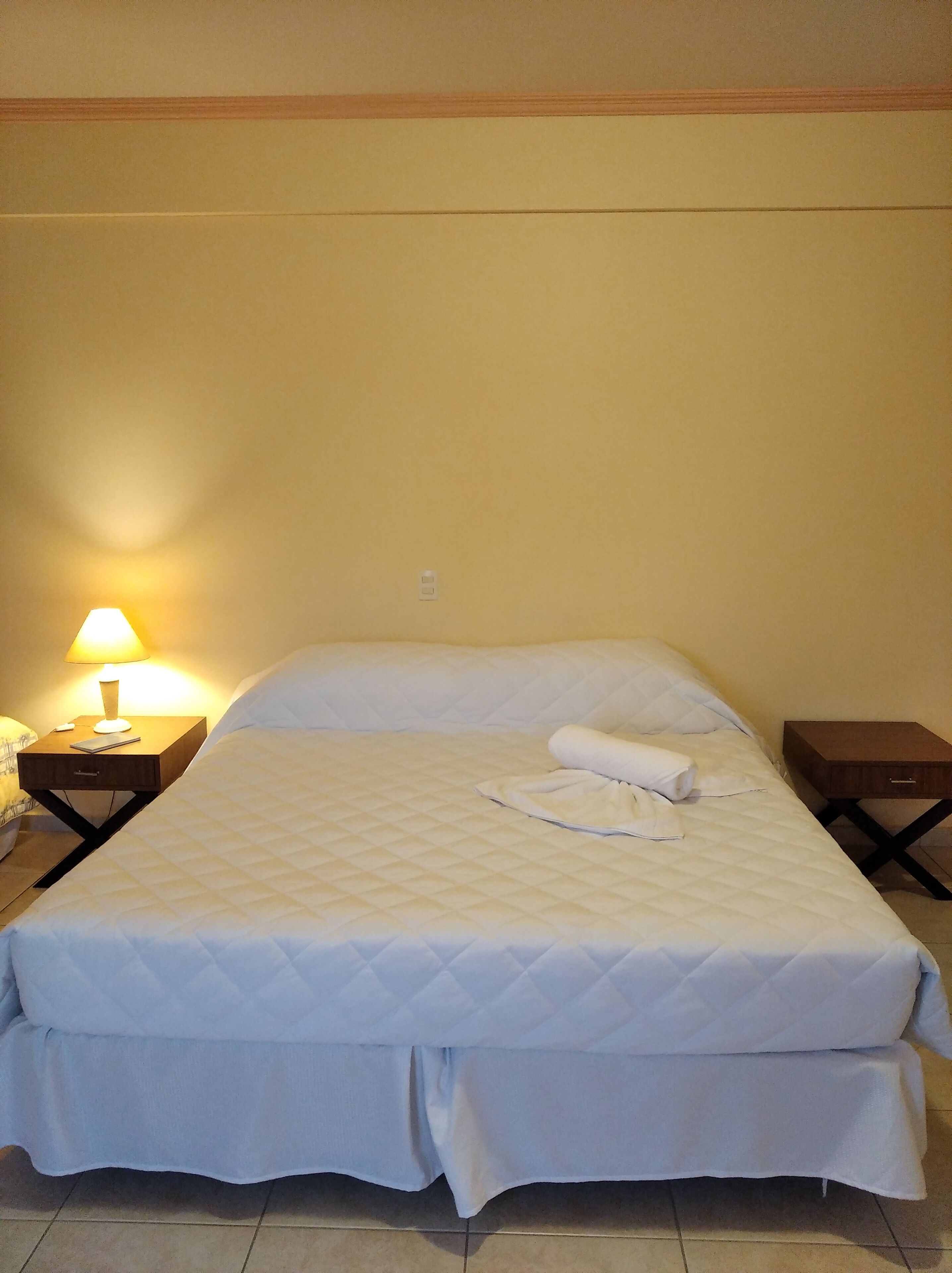 Una cama individual con edredón blanco acolchado, una lámpara de noche y una mesita de madera.