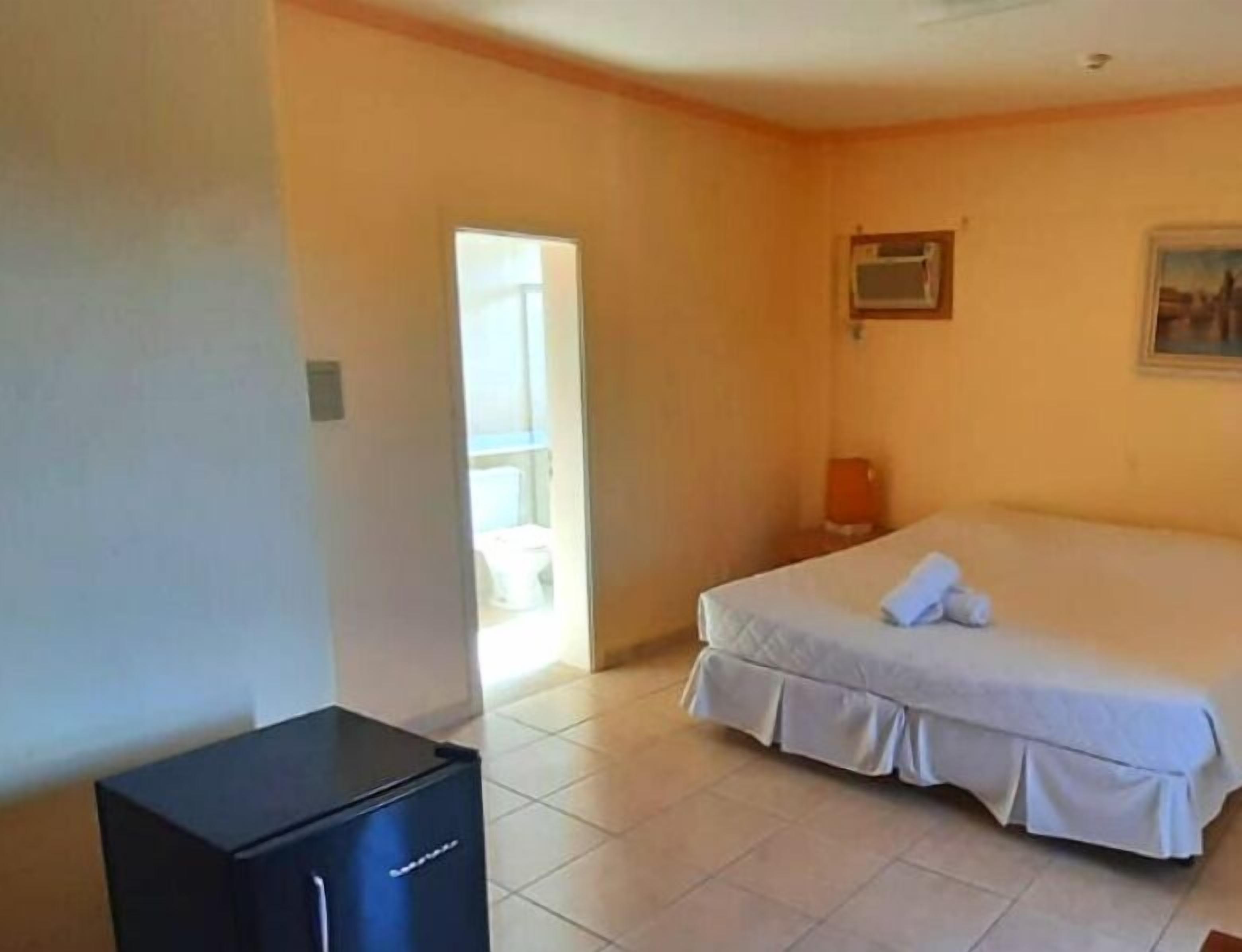 A hotel room with a bed, a small desk, a window, and a door leading to a bathroom.